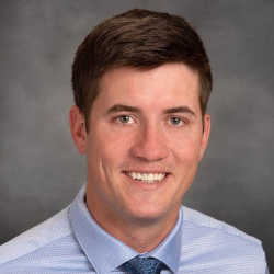 Pearson Wientjes, a man with short brown hair, wearing a light blue shirt and a blue tie, smiles against a gray background.