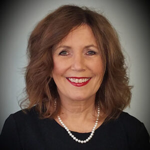 A woman with shoulder-length brown hair, wearing a black top and pearl necklace, smiles at the camera. The soft gray gradient in the background complements Karen Marshall’s elegant presence perfectly.